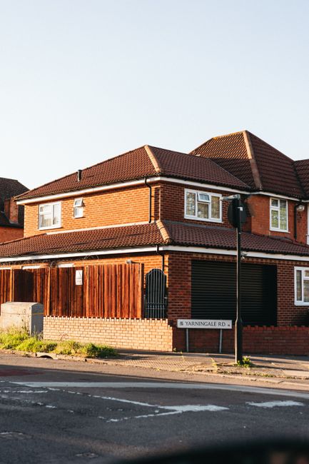 A two-storey brick house with a brown tiled roof situated on Yarningale Road, featuring white-framed windows and a black door, surrounded by a wooden fence on the side. In front of the property, there is a sidewalk adjacent to a paved road, with a tall black street lamp near the corner. The house appears to be part of a residential area, and the image captures the exterior during daylight, highlighting the typical setting for home relocation or moving services such as those offered by Man with Van Marks Gate, especially when facilitating furniture transport and packing during house removals in the Barking and Dagenham area.
