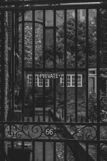 A black metal gate with vertical bars and decorative scrollwork at the bottom, partially obscuring a view of a residential area through the bars. Attached to the gate is a small sign reading 'PRIVATE,' indicating restricted access. The gate is positioned at the entrance of a property, with a pathway visible beyond, leading to houses with multiple windows and surrounding greenery. The scene is outdoors, captured during daytime with natural light reflecting off the metal surface. This image relates to house removals and moving services, emphasizing secure property access in the context of local home relocations, such as those undertaken by Man with Van Marks Gate during furniture transport or packing and moving processes.